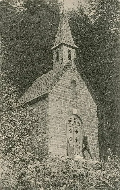Vor der St. Josephs-Kapelle steht ein Wanderer mit Wanderstock.